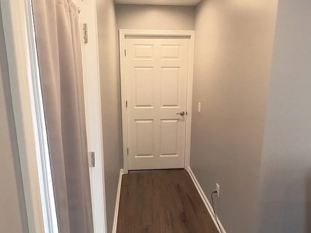 Hallway with gray walls and wood flooring, leading to a white door, in a newly remodeled in-law suite designed for elder family member care.