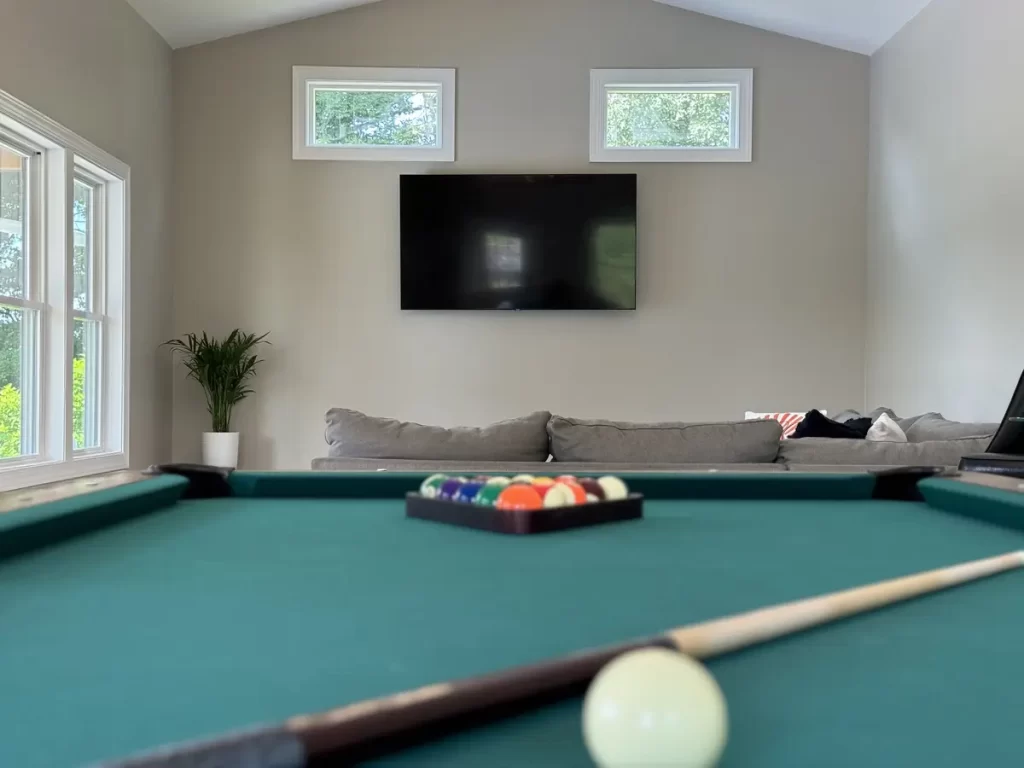 Interior view of the pool house addition in Akron, NY, showcasing a pool table and sectional sofa with a mounted TV in the background by Stately General Contracting.