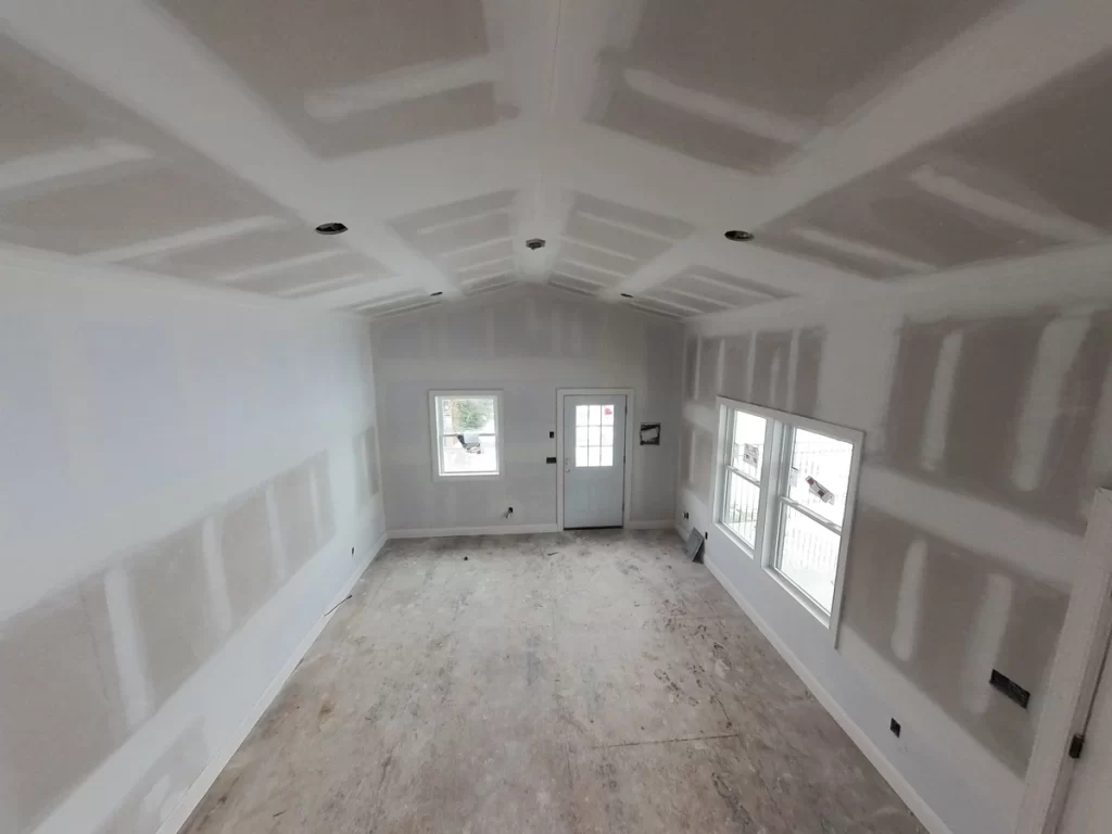 Partially constructed pool house interior with drywall and large windows.