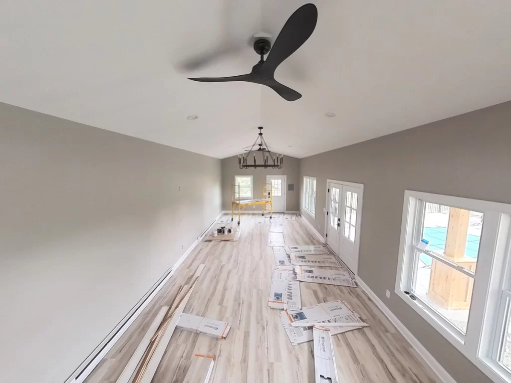 Interior pool house view with new flooring installation in progress and a large chandelier.