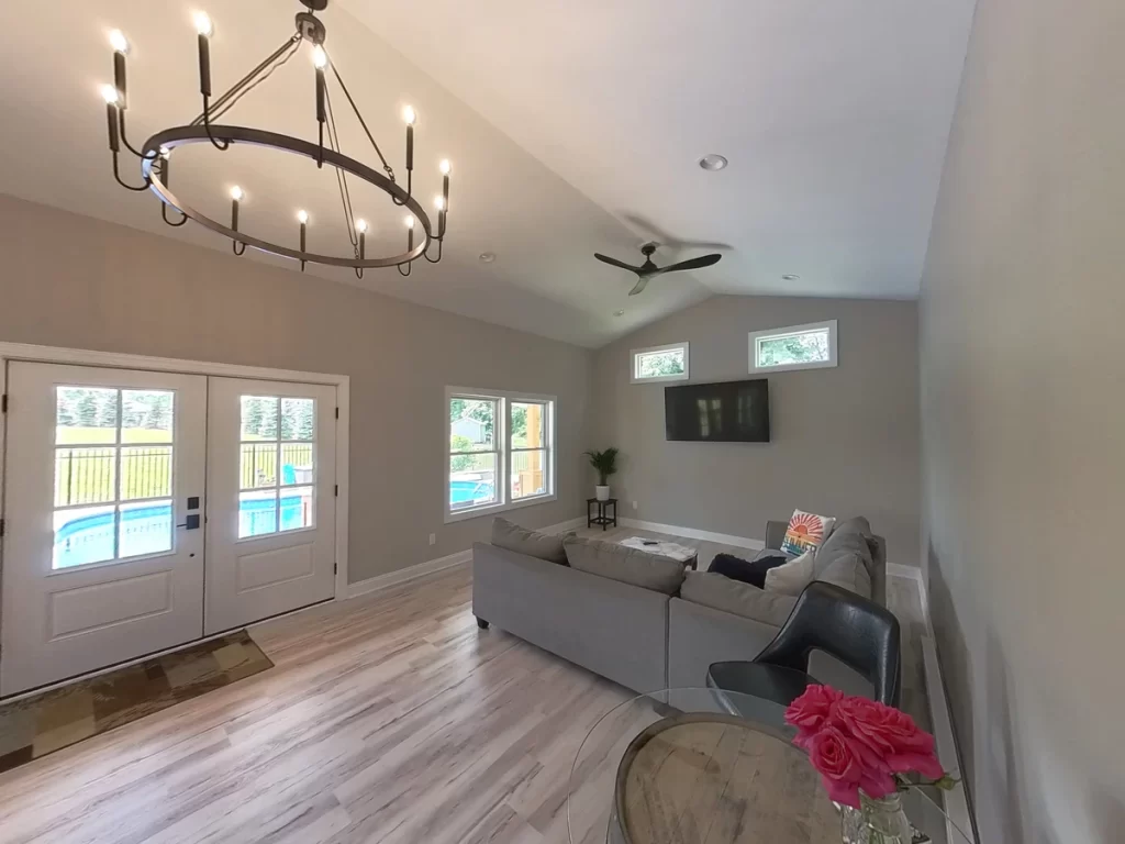 Spacious interior of the pool house addition in Akron, NY, featuring a chandelier, sectional sofa, and large windows by Stately General Contracting.