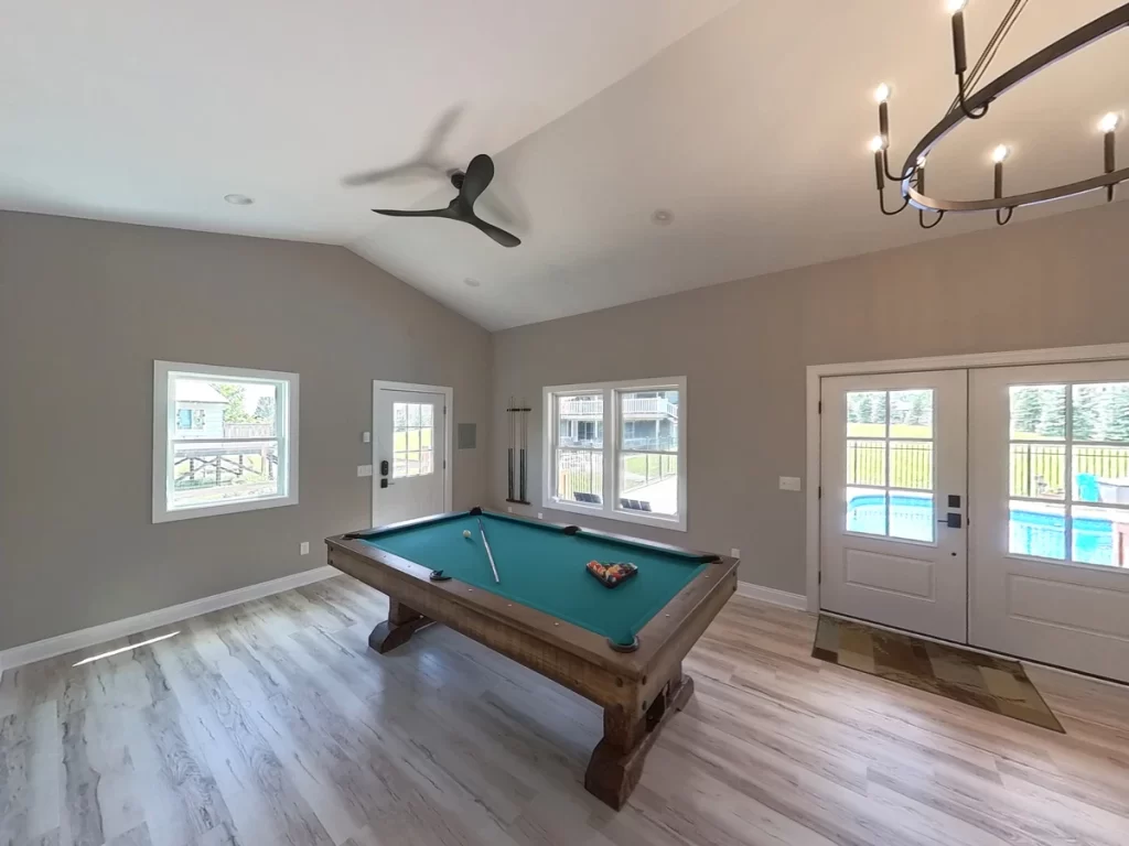 Wide-angle view of the pool house addition in Akron, NY, highlighting the pool table and double doors opening to the pool, designed and built by Stately General Contracting.