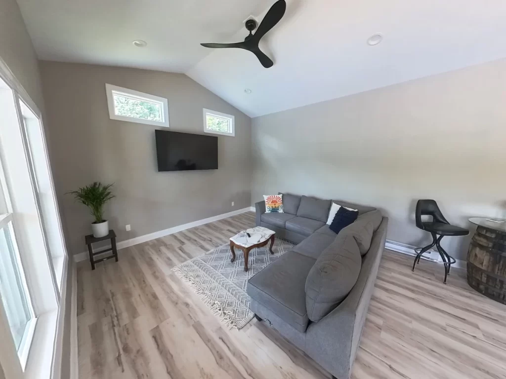 Interior view of the pool house addition in Akron, NY, highlighting the sectional sofa, TV, and ceiling fan by Stately General Contracting.