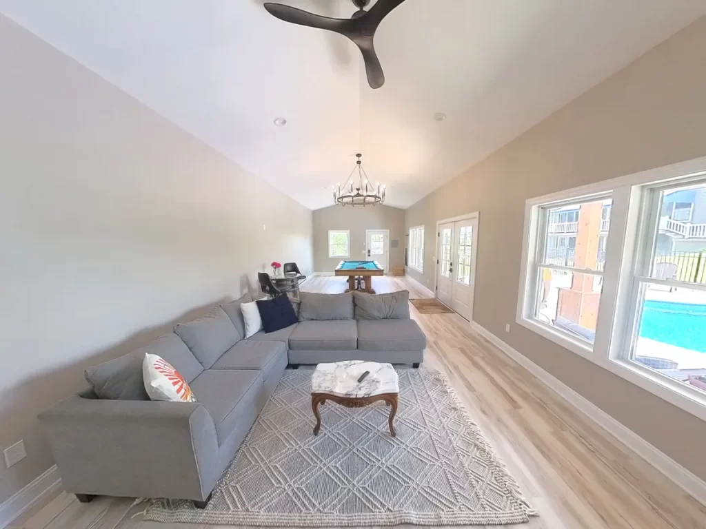 Wide-angle interior shot of the pool house addition in Akron, NY, showcasing the open layout with a sectional sofa and pool table, a project by Stately General Contracting.