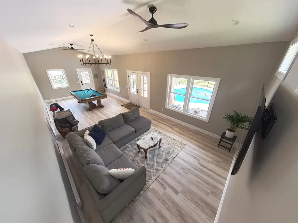 Interior view of the pool house addition in Akron, NY, with a sectional sofa, pool table, and view of the pool through the windows, designed by Stately General Contracting.