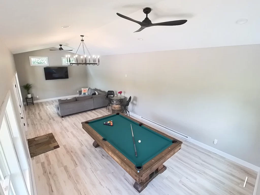 Pool house addition in Akron, NY, showing a pool table, sectional sofa, and ceiling fans, illustrating the spacious design by Stately General Contracting.