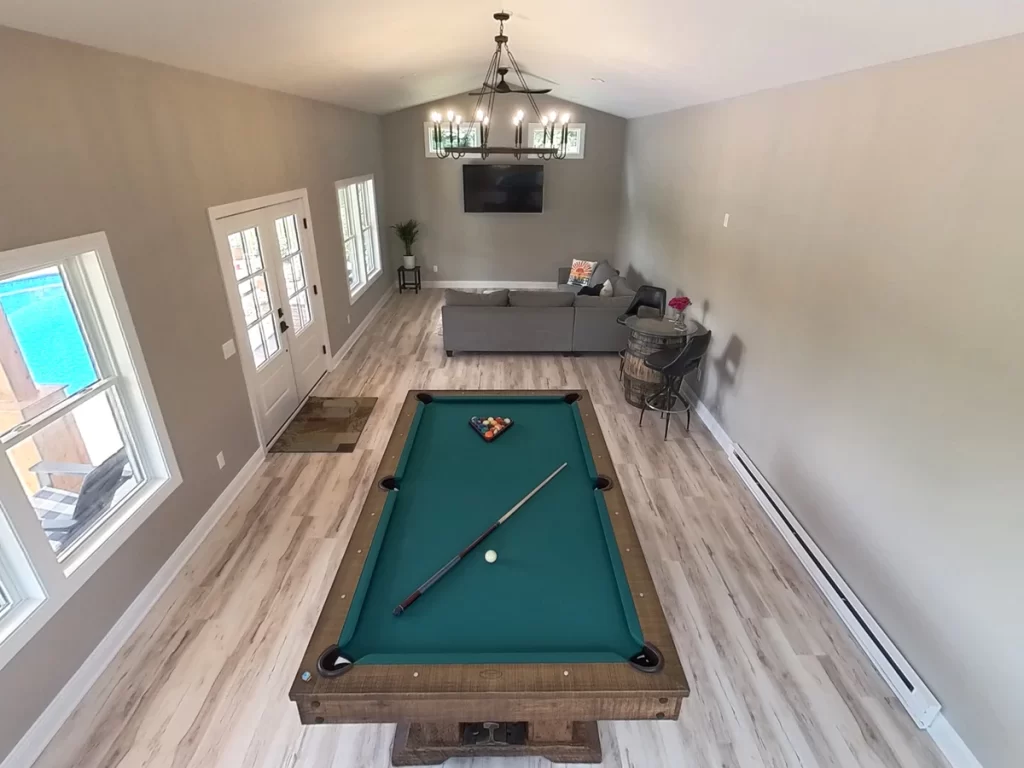 Long view of the pool house addition in Akron, NY, focusing on the pool table and the open space leading to the pool area, a project by Stately General Contracting.