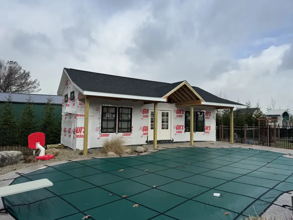 Pool house exterior wrapped in Guy's Lumber building paper, ready for siding installation, with a covered pool in the foreground.