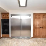 Old kitchen with large stainless steel refrigerator and wooden pantry doors.