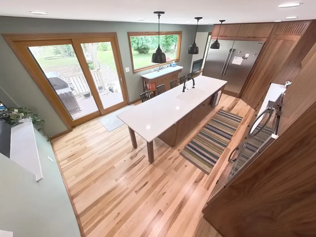 Dining area adjacent to remodeled kitchen by Stately Kitchen and Bath featuring a large wooden table and modern lighting.