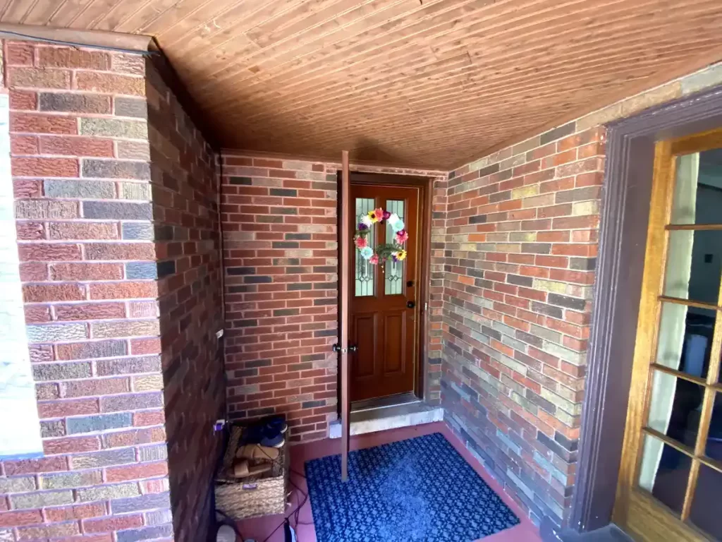 Rear porch entry of a Buffalo, NY home with brick walls and a wooden door before remodeling.