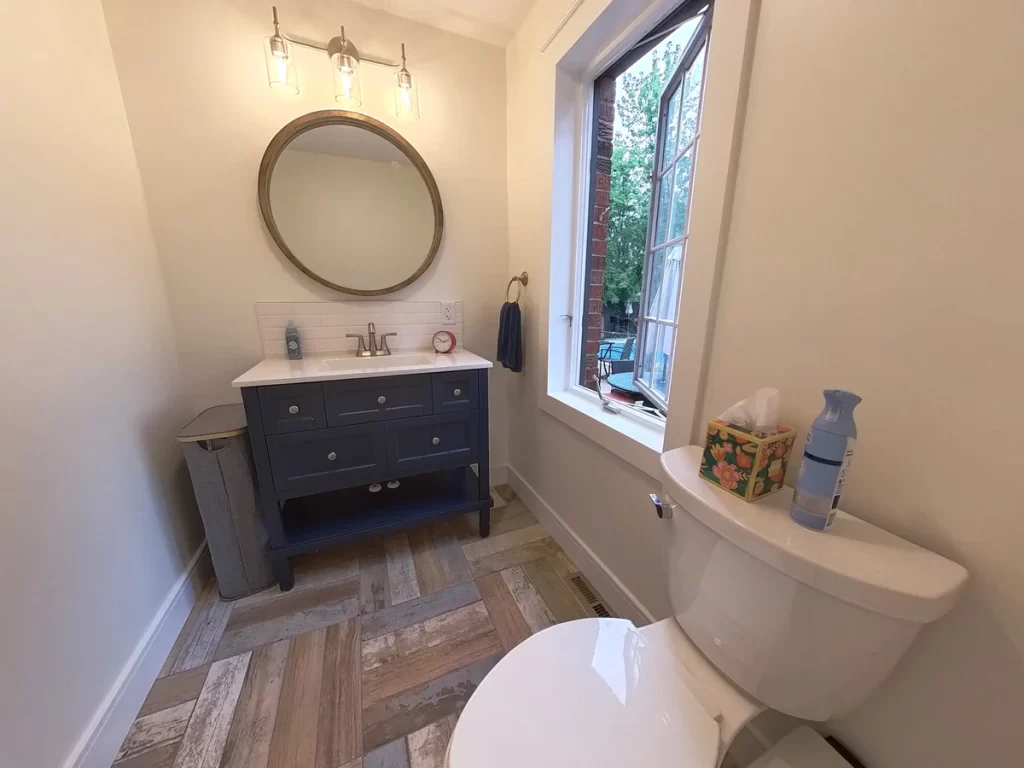 Renovated bathroom with dark vanity, round mirror, and modern lighting in Amherst, NY by Stately Kitchen and Bath.