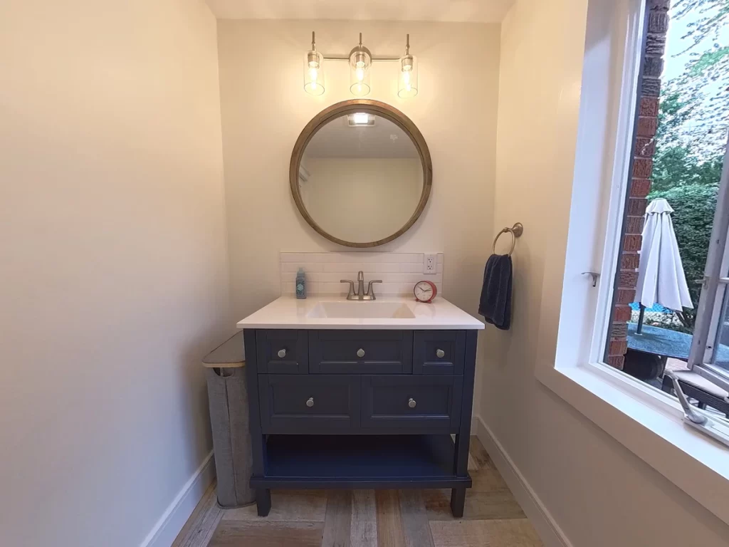 Bathroom vanity with round mirror and open window in Amherst, NY after renovation by Stately Kitchen and Bath.