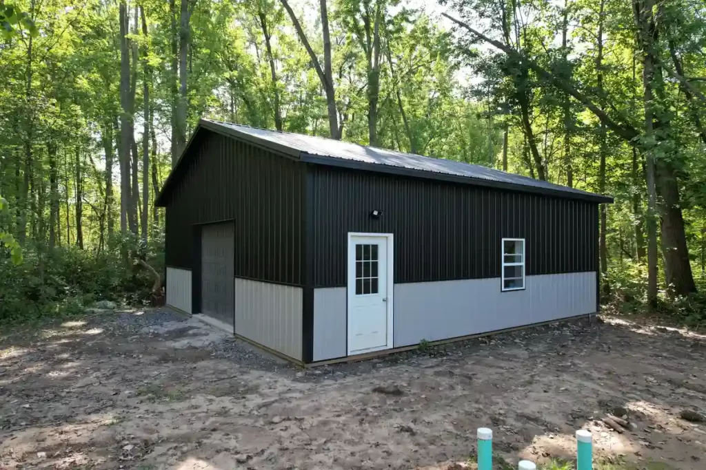 Side view of a black and gray pole barn in Clarence, NY, nestled in a wooded area, showcasing its spacious design and energy-efficient windows.