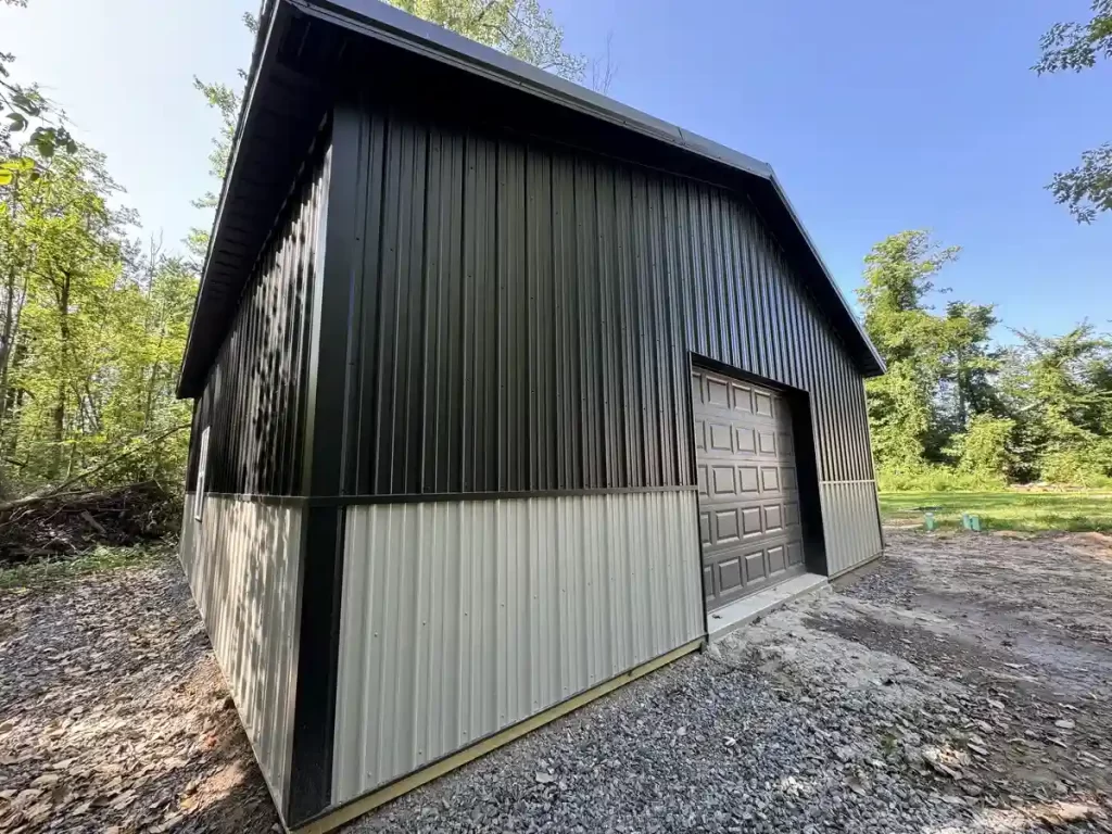 Wide-angle view of a black and gray pole barn in a wooded area of Clarence, NY, illustrating the modern dual-tone exterior and spacious interior.