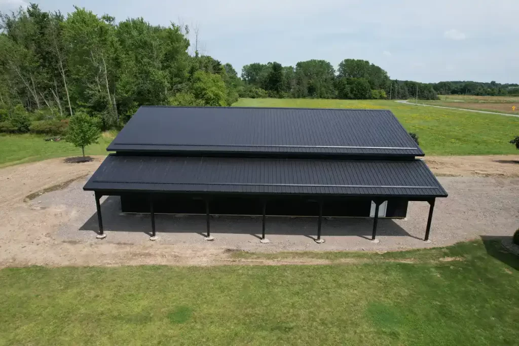 Aerial shot of a custom-built matte black pole barn in Clarence, NY, showcasing the barn's extended roofline and high-quality Everlast II Steel Panels.