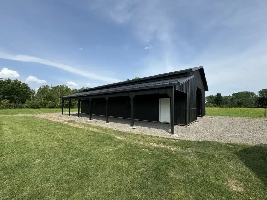 Side view of a matte black pole barn in Clarence, NY, featuring a covered porch area, built with durable Everlast II Steel Panels by Stately Pole Barns.