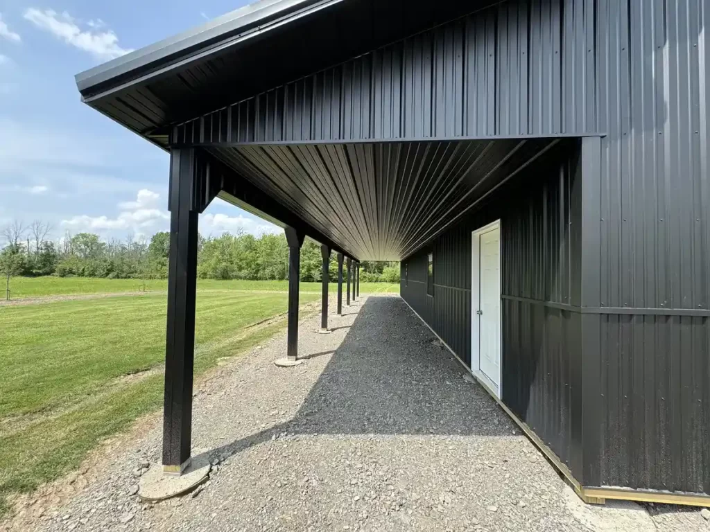 Close-up of the covered porch area of a matte black pole barn in Clarence, NY, highlighting the precision-engineered roofing and structural support.