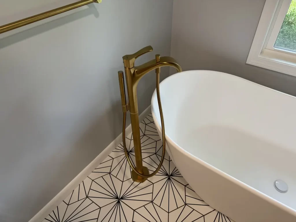 After photo of a modern bathroom featuring a freestanding tub with brass fixtures and geometric tile flooring.