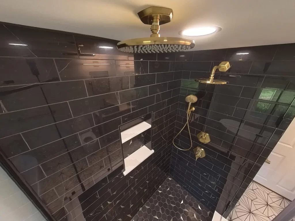 Detailed shot of a luxurious walk-in shower with black tile, hexagonal flooring, brass fixtures, and a large rain showerhead.