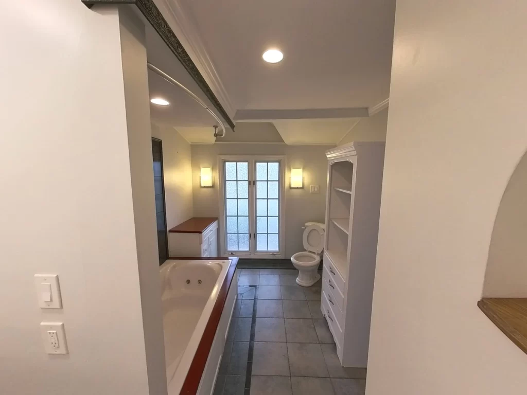 Before photo of a bathroom with a whirlpool tub, outdated cabinetry, and tile flooring.