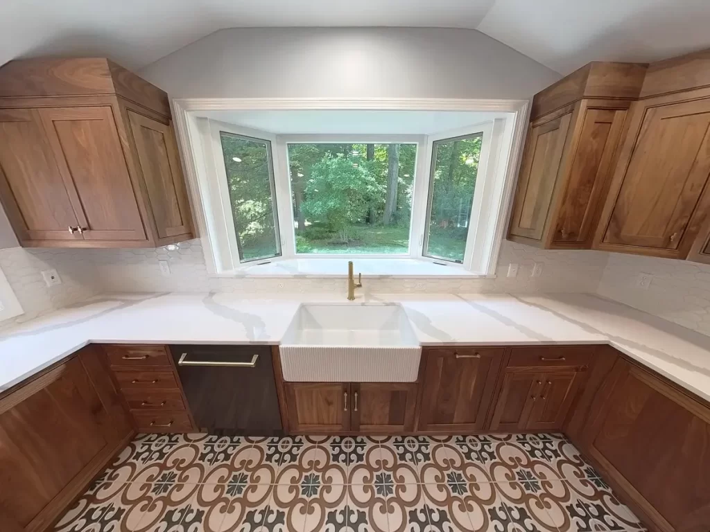 Close-up of remodeled kitchen sink area in Elma, NY, featuring custom wooden cabinets, a farmhouse sink, and a large window with a view.