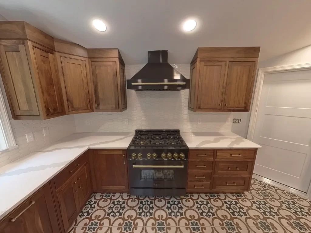 Close-up of remodeled kitchen range and oven area in Elma, NY, featuring custom wooden cabinets and sleek range hood.