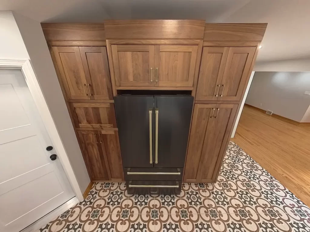 Closed cabinet view in remodeled kitchen in Elma, NY, highlighting black refrigerator with brass accents and custom wood cabinetry.