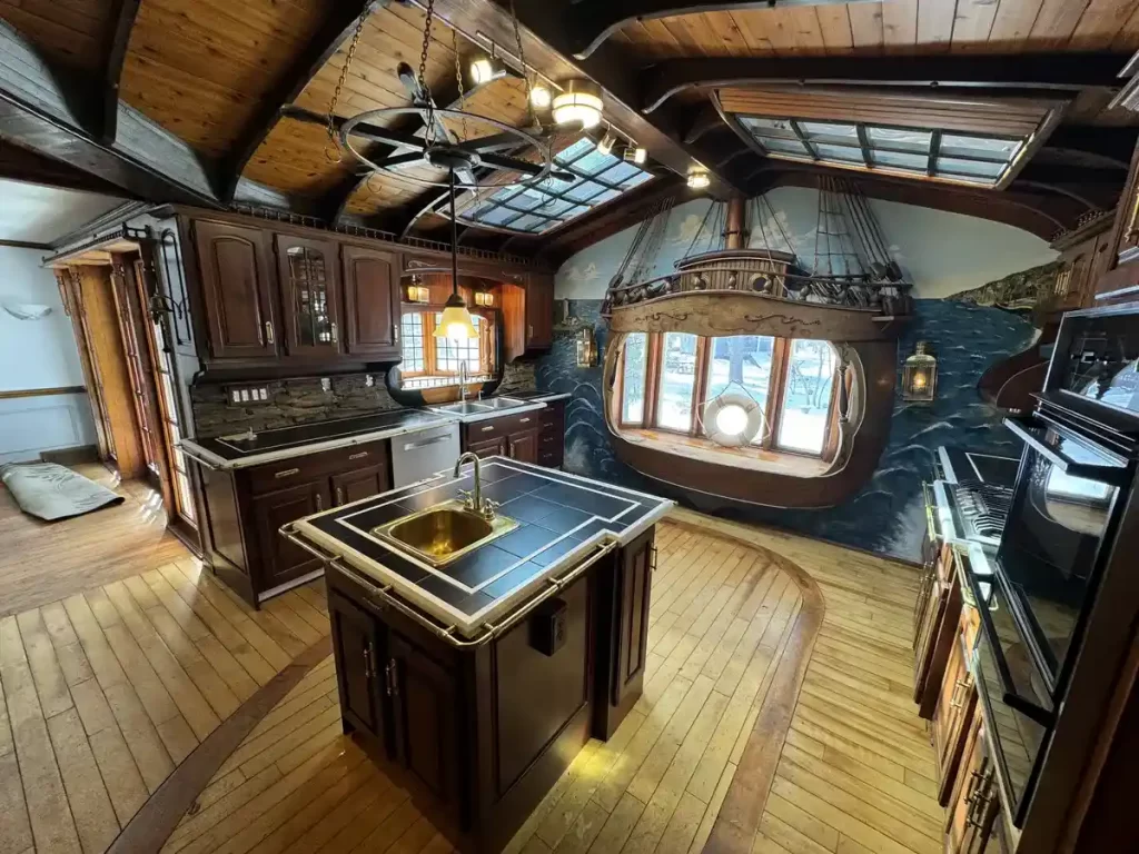 Before remodel image of a ship-themed kitchen in Elma, NY, showcasing extensive wooden cabinetry, faux ship stern, and skylights.