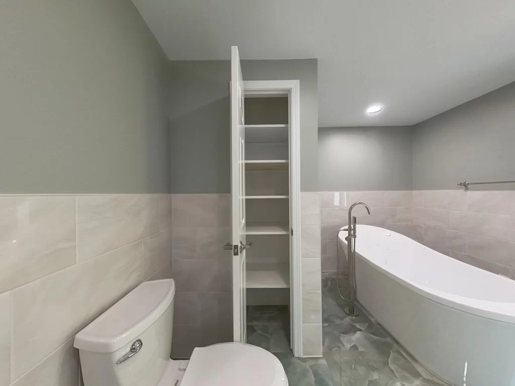 View of a modern bathroom featuring a toilet, freestanding bathtub, and built-in closet shelves for additional storage. Remodel by Stately Kitchen and Bath.