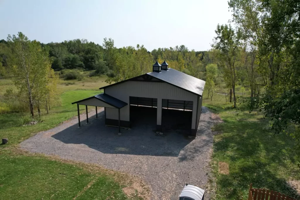 Aerial view of a finished Stately Pole Barn with black roofing, two cupolas, and surrounding green landscape.