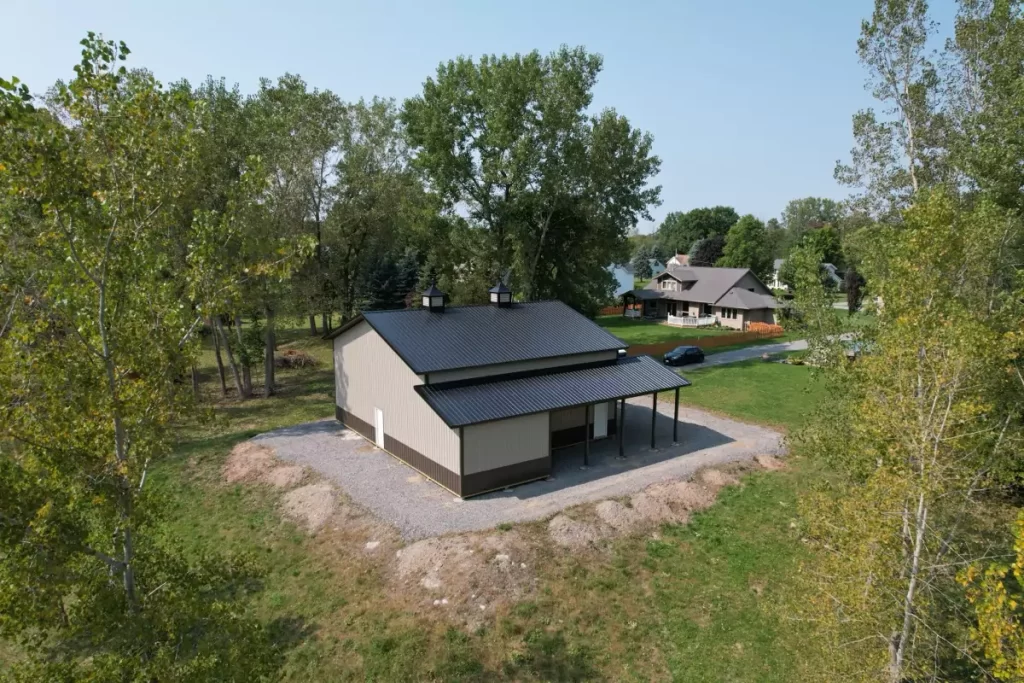 Aerial side view of a complete Stately Pole Barn with dual cupolas and open doors, set in a grassy area.