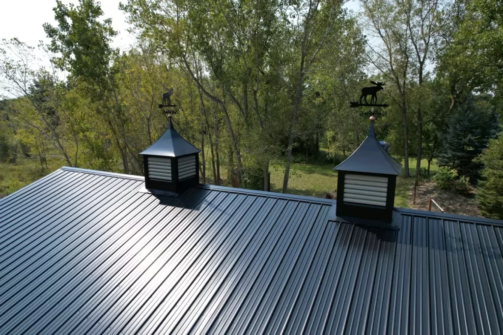 Close-up of the black metal roof and decorative cupolas of a Stately Pole Barn amidst a wooded background.