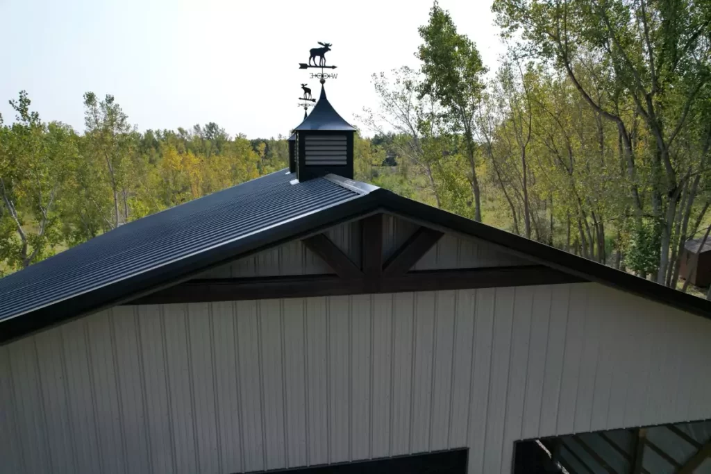 Close-up view of the black metal roof, decorative timber trim, and duel cupolas of a Stately Pole Barn.