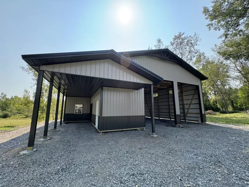 View of the side entrance and overhang of a Stately Pole Barn with a gravel driveway under bright sunlight.