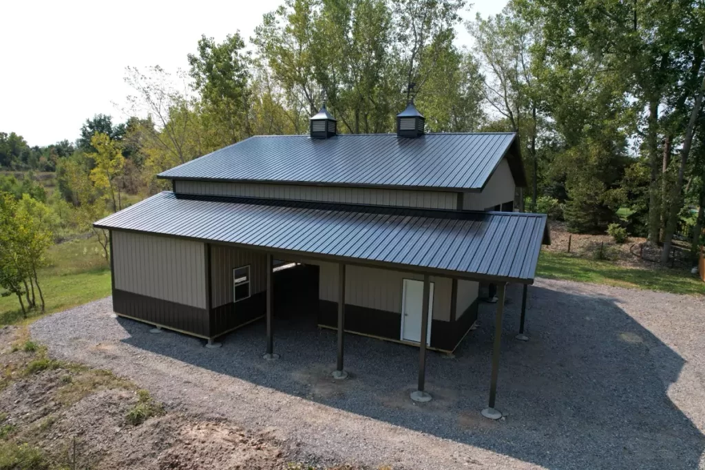 Side view of a newly constructed Stately Pole Barn with black roof and side overhang in a rural setting.