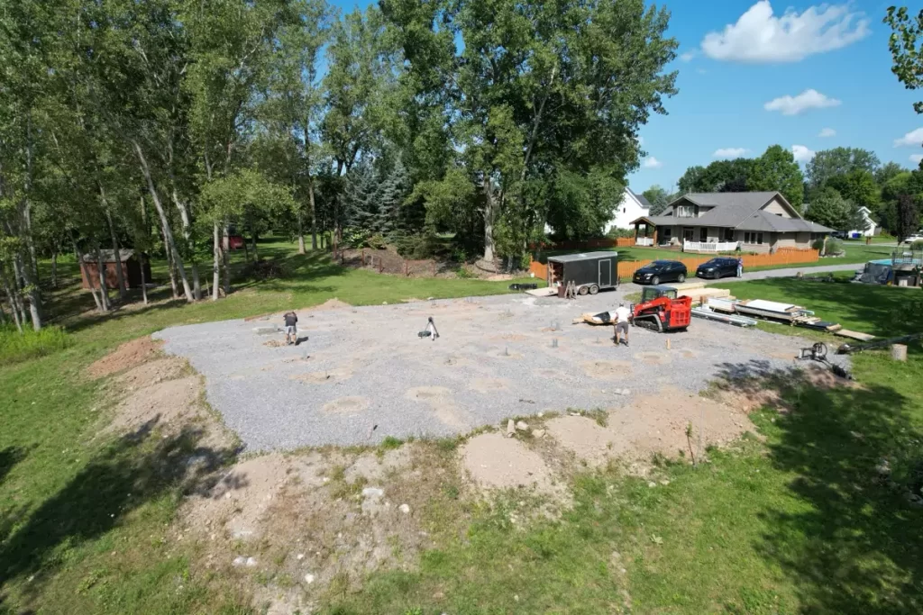 Stately Pole Barn construction site showing foundation piers before post-frame assembly, with tools and equipment in view.