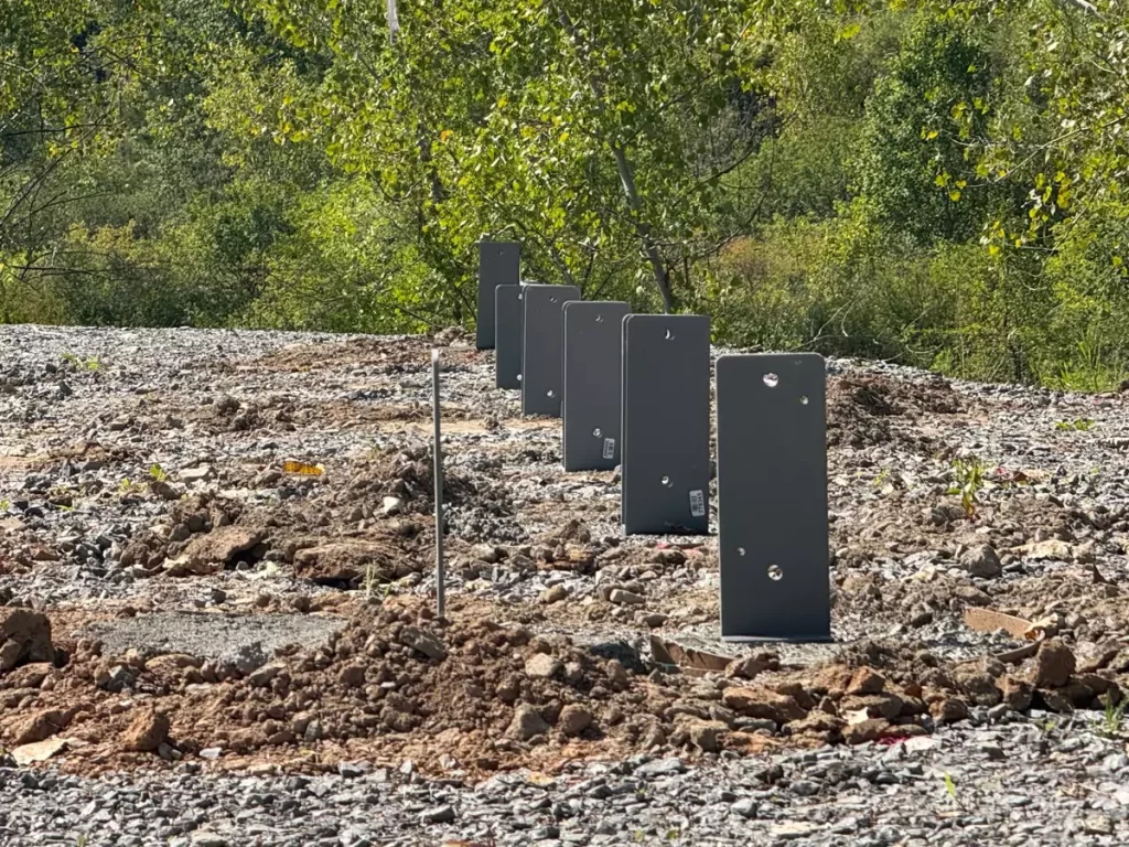 Close-up of Perma-Column® foundation brackets at Stately Pole Barn construction site, showing post anchors in gravel.