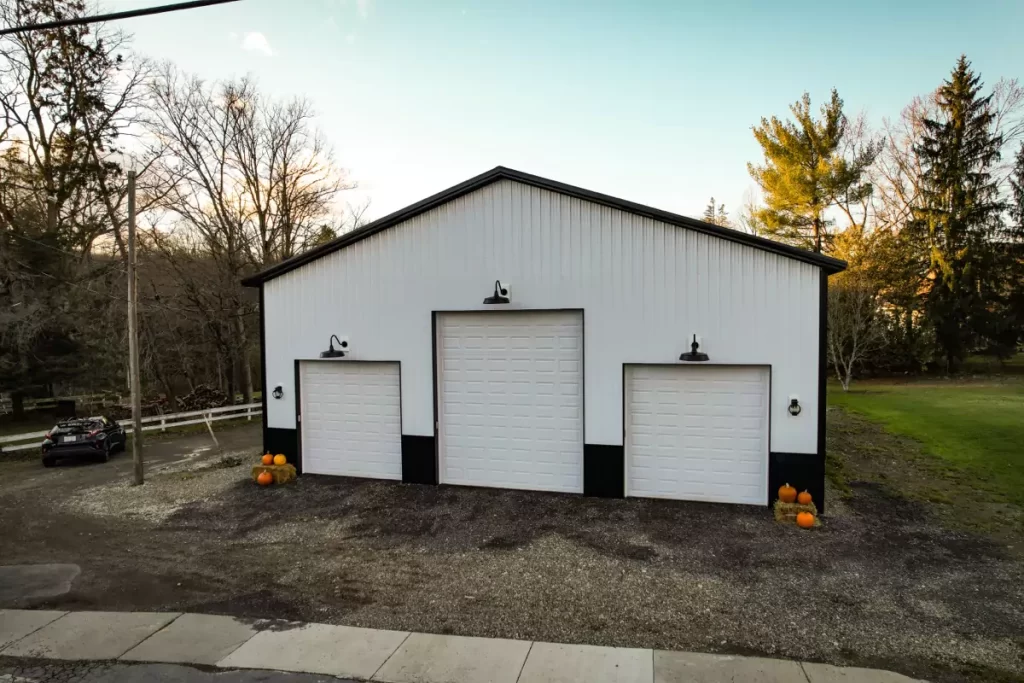 Front view of a Stately-built modern pole barn in Holland, NY, with three garage doors, pumpkins, and black trim showcasing craftsmanship.