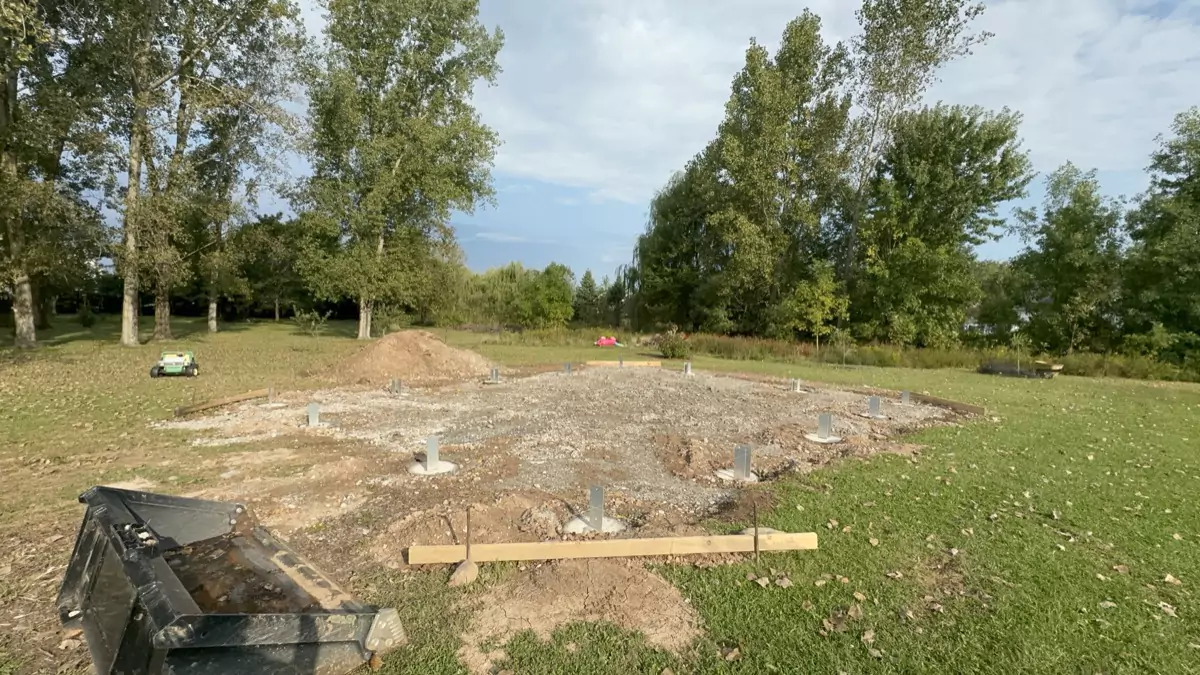 Wide view of the pole barn construction site with concrete piers set, preparing for framing and structural support.