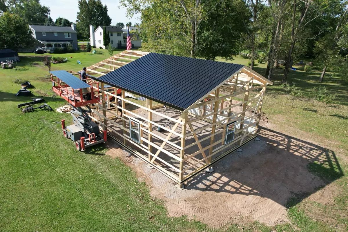 Workers completing framing of Stately Pole Barn with black metal roofing partially installed on the structure.