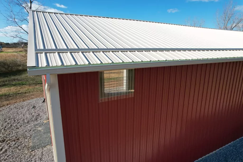 Close-up of vented ridge cap, snow bar, and transom window on red pole barn, designed for optimal ventilation and structural strength.