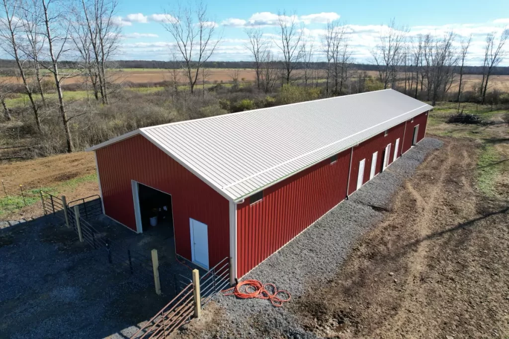 Side angle of the agricultural pole barn, featuring multiple white panel doors and clean, gravel-lined perimeter.