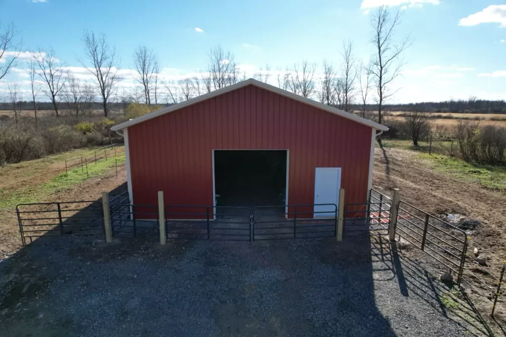 Front view of a pole barn with a wide overhead door and man door, highlighting customizable entryways and durable materials.