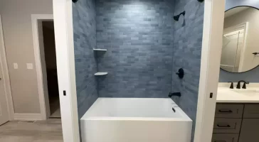 Deep bathtub and sleek blue tile surround with black fixtures by Stately Kitchen and Bath in Orchard Park, NY.