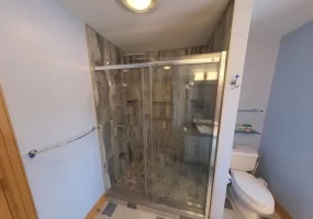 After renovation, an inviting walk-in shower with clear glass door, modern gray tile design, and high-quality fixtures is the centerpiece of this bathroom, highlighting the expertise of Stately Kitchen and Bath in delivering stylish and practical bathroom transformations.