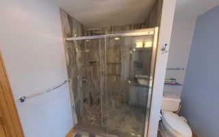 After renovation, an inviting walk-in shower with clear glass door, modern gray tile design, and high-quality fixtures is the centerpiece of this bathroom, highlighting the expertise of Stately Kitchen and Bath in delivering stylish and practical bathroom transformations.