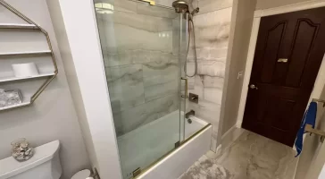 Glass-paned sliding shower door with gold accents.