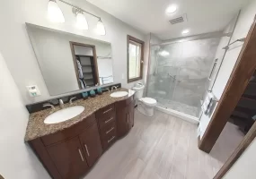 Modern bathroom remodel by Stately Kitchen and Bath in Gettzville, NY, featuring a double vanity with granite countertops, large mirror, and a spacious glass-enclosed shower.