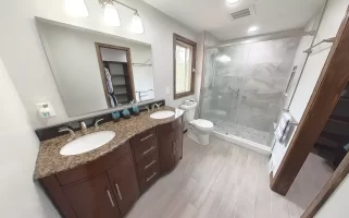 Modern bathroom remodel by Stately Kitchen and Bath in Gettzville, NY, featuring a double vanity with granite countertops, large mirror, and a spacious glass-enclosed shower.